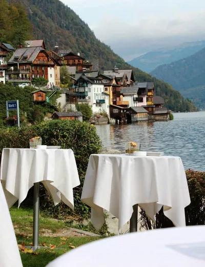 Cocktail tables set up for a reception in the Kirchengarten in Hallstatt, with the town and lakeshore in the background, at Heritage.Hotel Hallstatt in the Salzkammergut