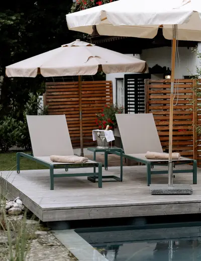 Natural pool at the Schlosswirt zu Anif (c) Gassner Gastronomie, HECHTFISCH Two lounge chairs under a beach umbrella at the natural pool at the Schlosswirt zu Anif (c) Photo: Gassner Gastronomie, HECHTFISCH