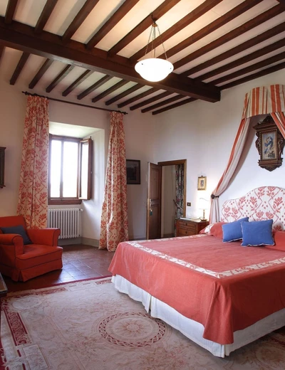 Wood-ceiling room and double bed with red throw at Villa le Barone in Tuscany