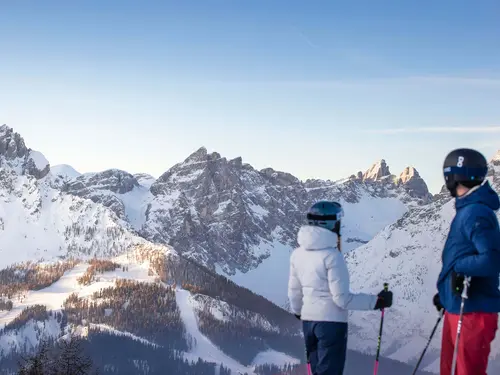 [Translate to English:] Zwei Skifahrer vor dem Dolomiten-Panorama mit den Drei Zinnen bei strahlend blauem Himmel (c) Foto Tourismusverband Innichen / Kottersteger