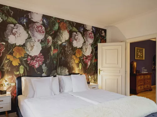 Zimmer mit grossen Blumenblüten auf der Rückwand des Doppelbettes und offener Türe zum Salon im Hotel Castel Rundegg in Meran, Südtirol