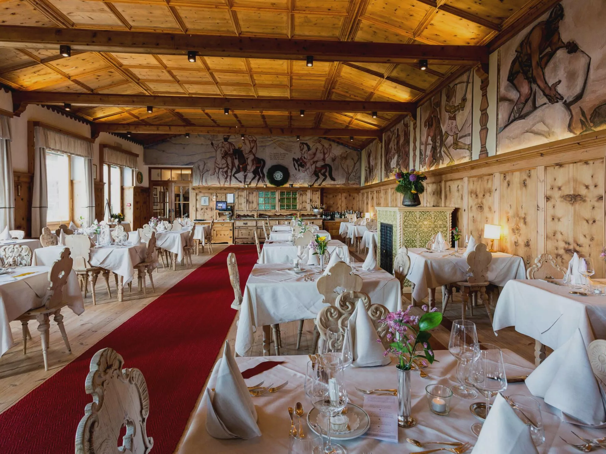 Riese Grimm dining room with wall fresco and festively set tables in the historic restaurant of Hotel Der Zirmerhof in Radein, South Tyrol.