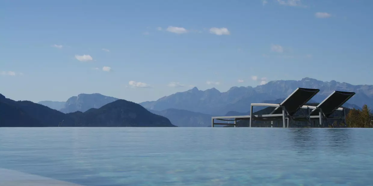 View from the Zirmerhof infinity pool of the surrounding mountain world, the blue of the water appearing to meld with the mountains and the blue sky.