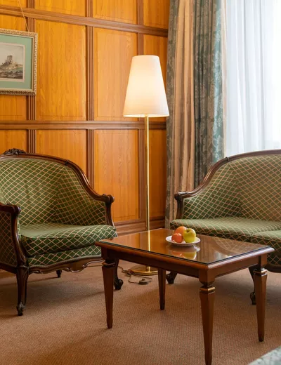 Salon-Ecke eines Zimmers im Stil der Wiener Klassik im Hotel König von Ungarn in Wien mit Stehlampe, Tisch, Fauteuil und Sitzbank sowie Holzvertäfelung