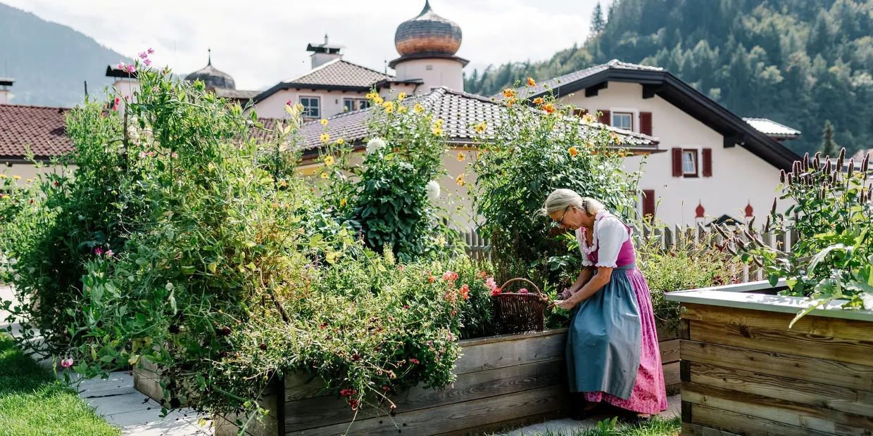 Sandra Moigg, Gasthof Herrnhaus (c) Sebastian Gabriel Sandra Moigg of Gasthof Herrnhaus wearing a dirndl, perched on the edge of a raised vegetable bed next to the herbs she grows herself (c) photo Sebastian Gabriel