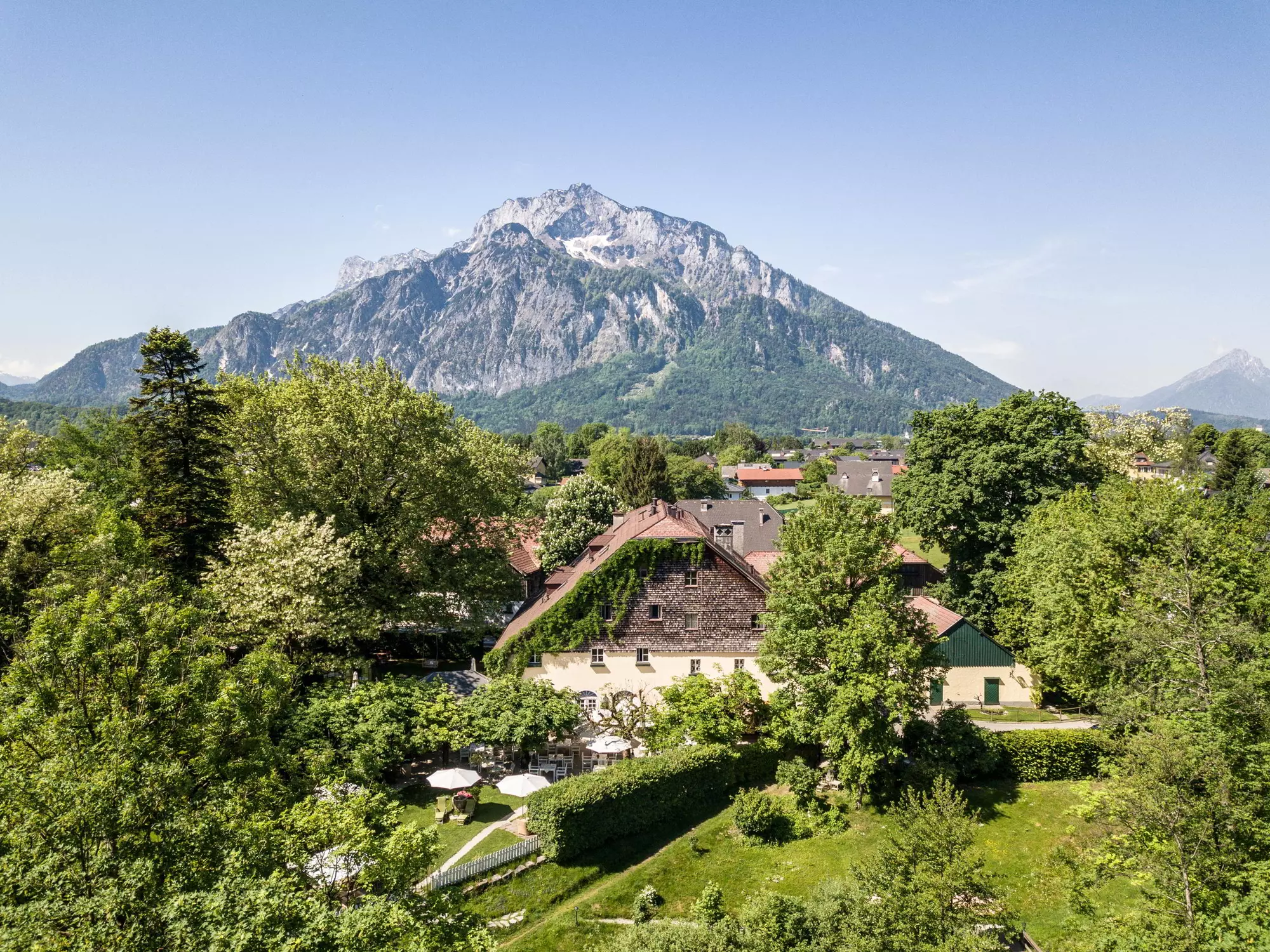 Aerial view of the Schlosswirt zu Anif in the middle of greenery with the Untersberg in the background (c) Photo Schlosswirt zu Anif