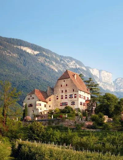 Schloss Englar auf einer Anhöhe, umgeben von Weingärten und alten Bäumen, mit Bergen im Hintergrund, Südtirol