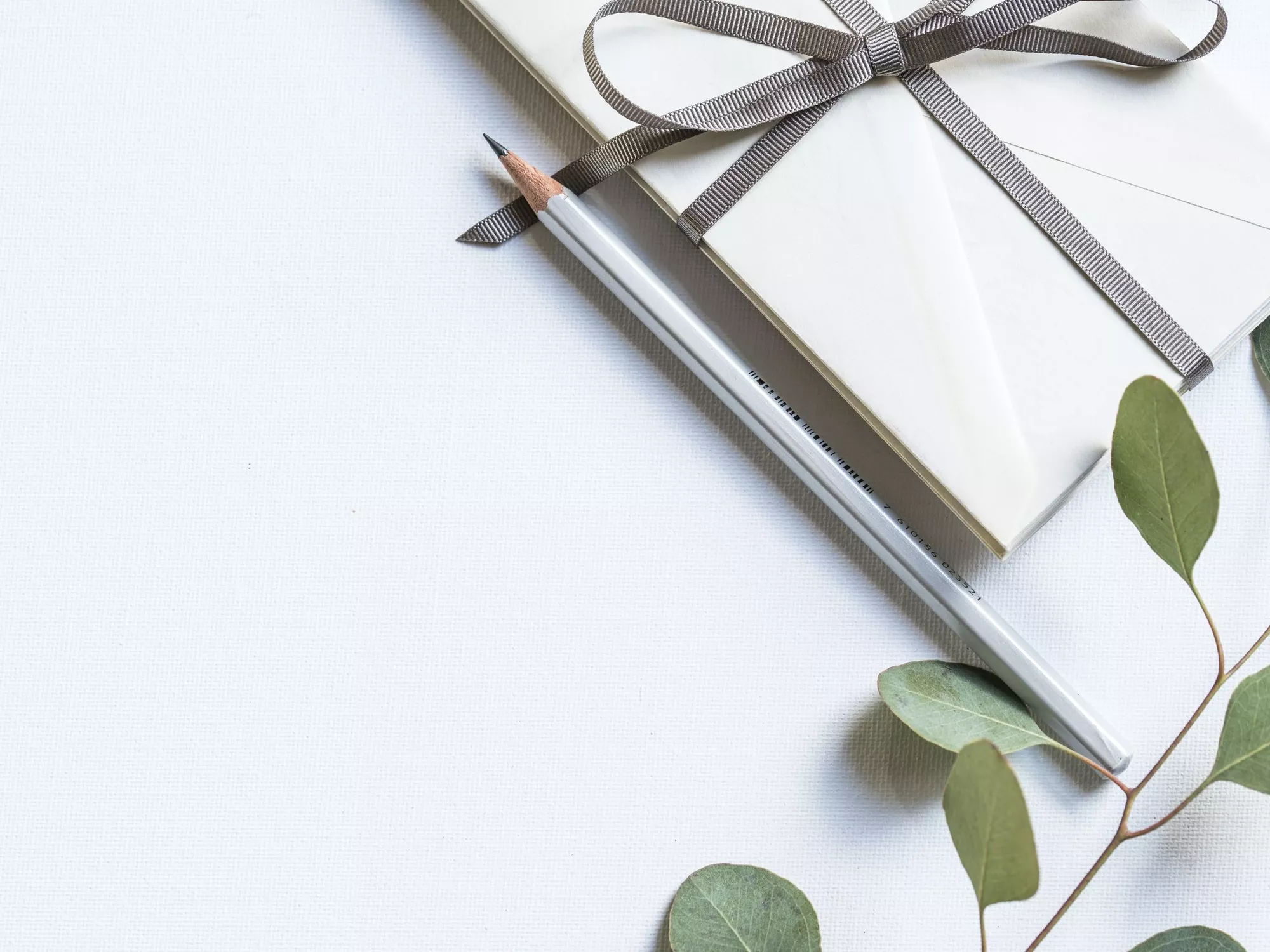 Weisses Kuvert mit Geschenksband, einem Bleistift und einem Zweig mit grünen Blättern zur Veranschaulichung eines Gutscheins (c) Foto Joanna Kosinska / Unsplash