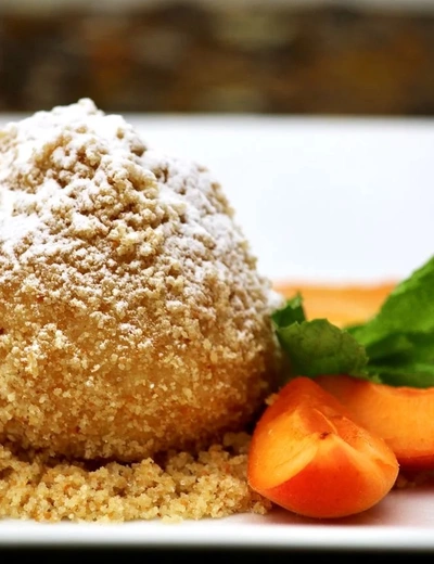 Close-up of an apricot dumpling sprinkled with sugar, accompanied by fresh apricot pieces and garnished with a mint leaf, served at Restaurant Hotel Richard Löwenherz