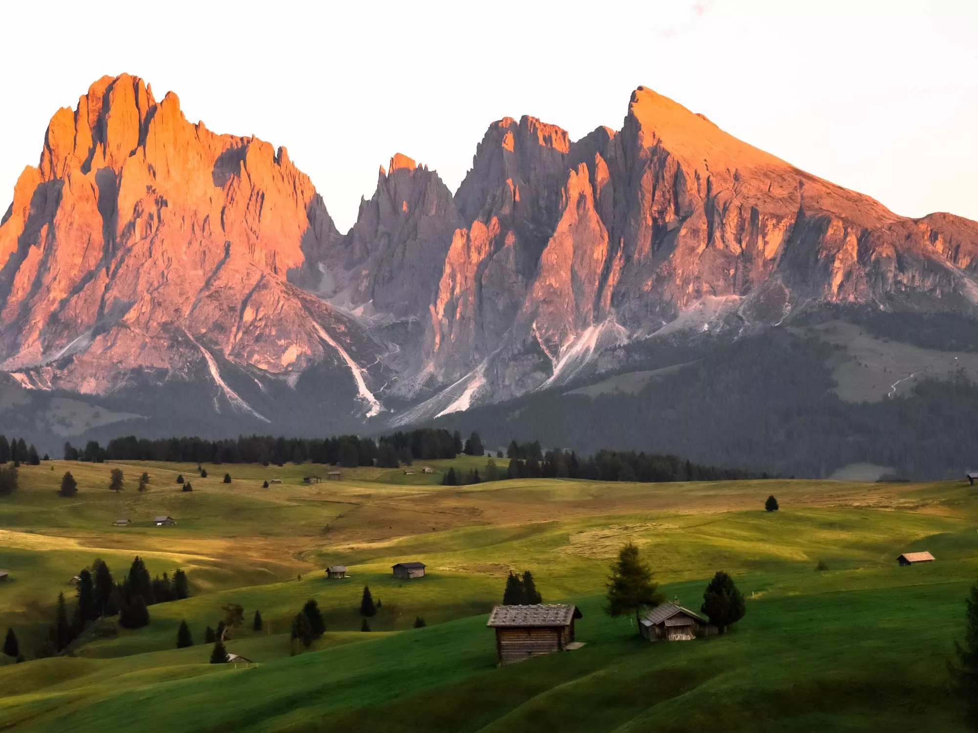 Green alpine meadows with wooden huts, the Dolomites in the background, at sunset (c) Tomas Malik / Unsplash