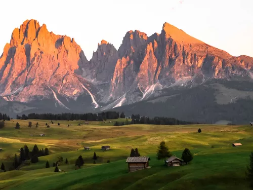 Green alpine meadows with wooden huts, the Dolomites in the background at sunset (c) Tomas Malik / Unsplash