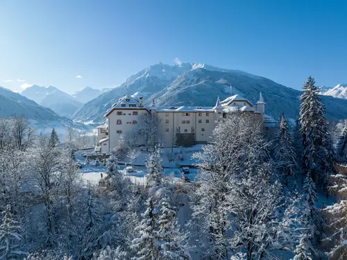Aerial view of Schloss Mittersill in winter surrounded by snow-covered mountains and forests under a cloudless sky (c) Photo Schloss Mittersill / Daniel Kogler