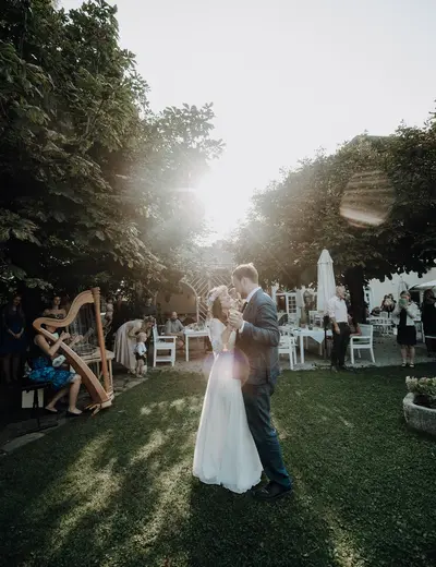 Tanzendes Hochzeitspaar im Garten vom Schlosswirt zu Anif, links im Bild eine Harfenspielerin, im Hintergrund die Hochzeitsgäste (c) Foto Claudia Weaver Photography