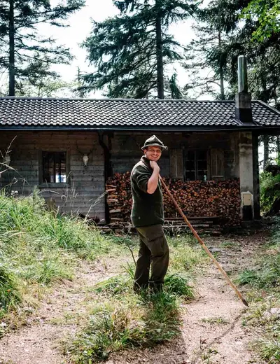 Maximilian Moigg, Gasthof Herrnhaus (c) Sebastian Gabriel Maximilian Moigg of Gasthof Herrnhaus wearing a hunting hat in front of a wooden cabin in the forest (c) photo Sebastian Gabriel
