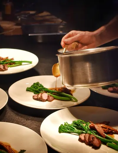 Supperclub (c) Ansitz Felsenheim Preparing for the Supper Club: Several white plates with a meat dish, sauce being added to one of them (c) photo Ansitz Felsenheim
