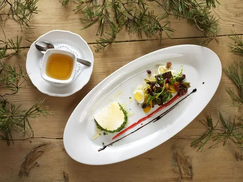 Fresh sheep’s cheese with salad, presented on a white plate, served on a natural-wood table at Landgasthof Linde, photo Herbert Lehmann